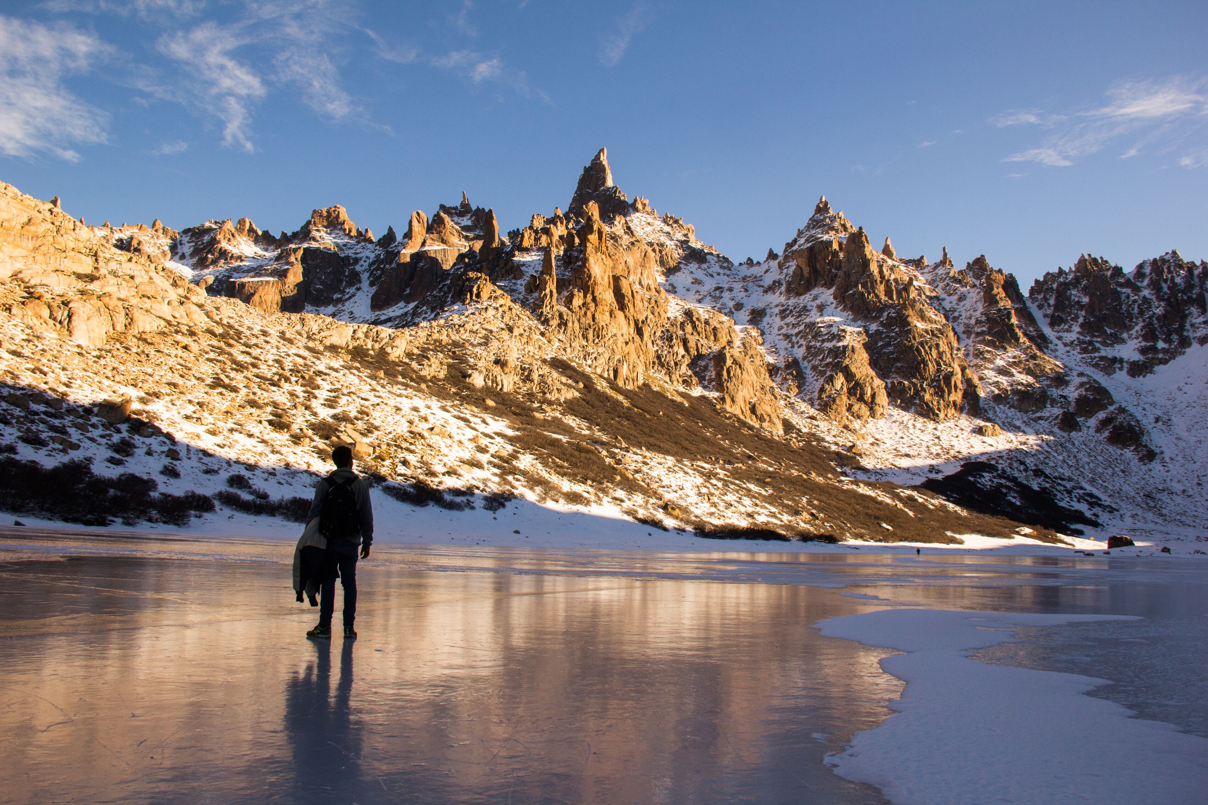 Una persona caminando sobre un lago helado, con montañas nevadas al fondo.