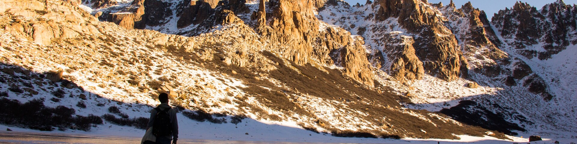 Una persona caminando sobre un lago helado, con montañas nevadas al fondo.