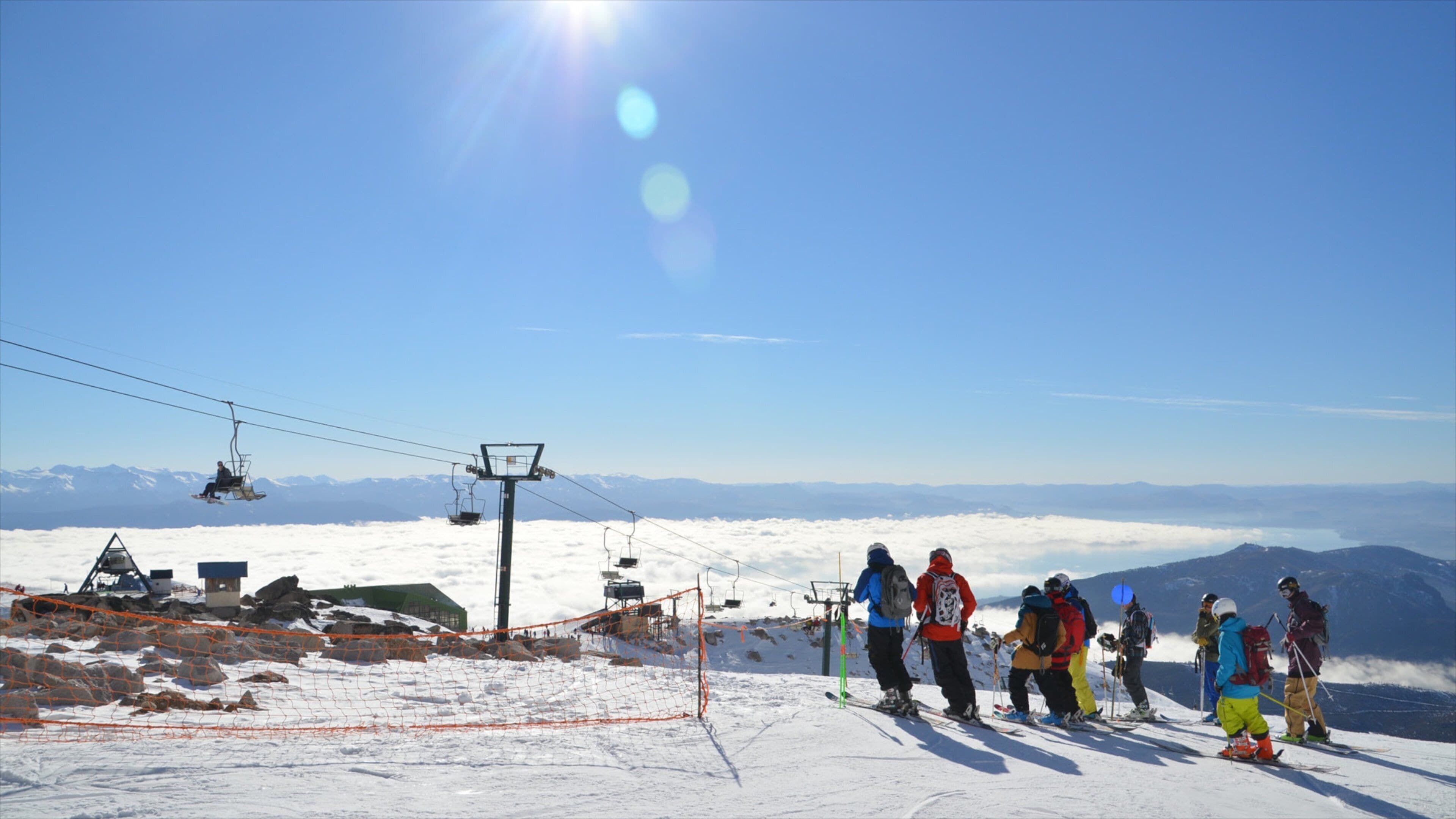Una pista de esquí con esquiadores, un telesilla y montañas nevadas al fondo.