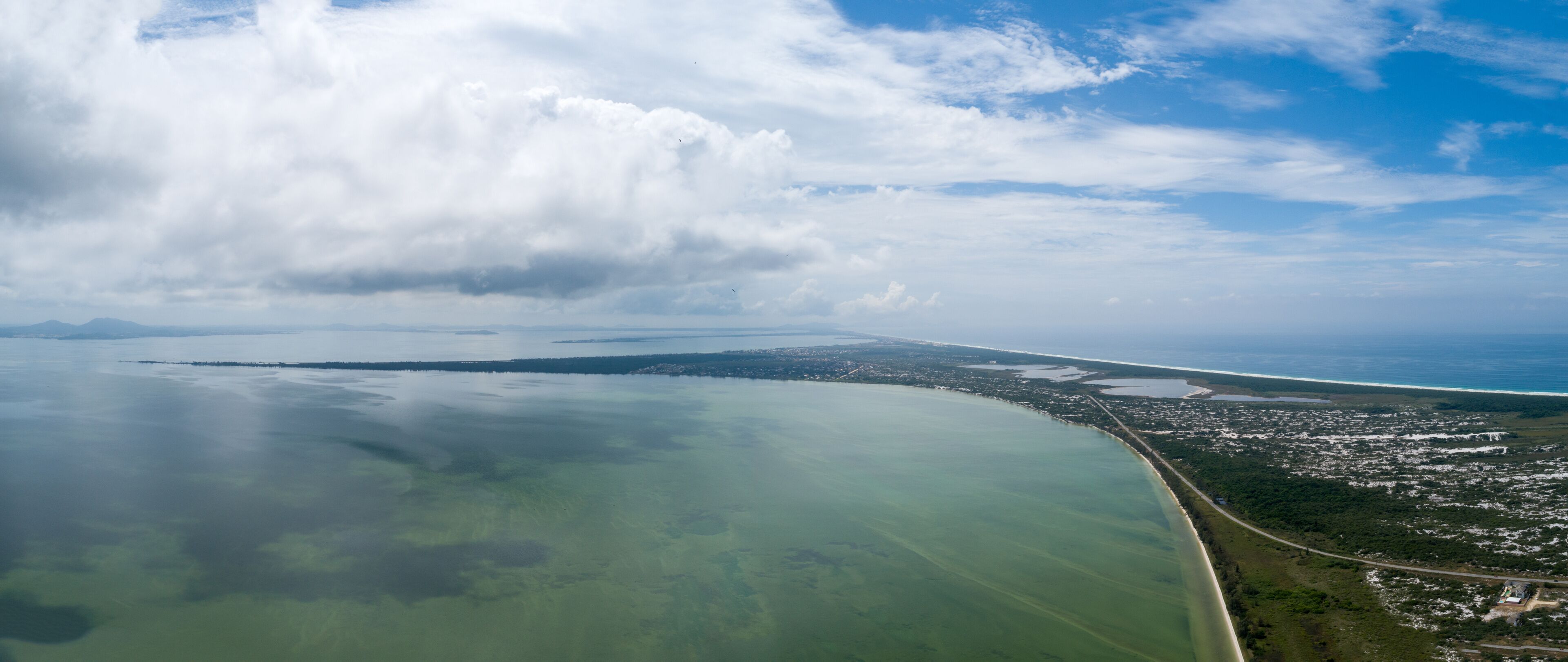 A coastal landscape with a large body of water, a curved shoreline, and a distant cityscape.