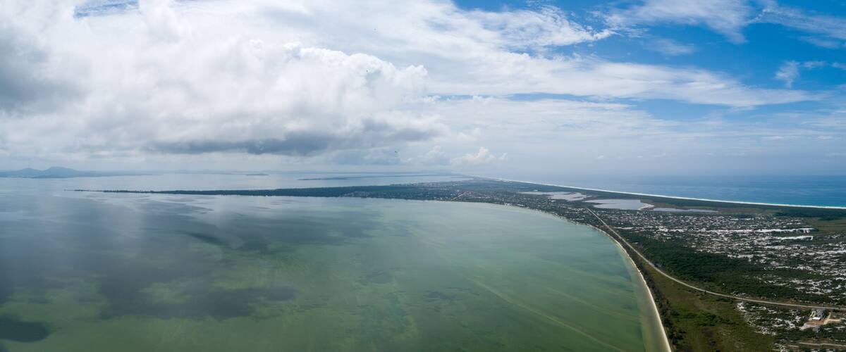 A coastal landscape with a large body of water, a curved shoreline, and a distant cityscape.