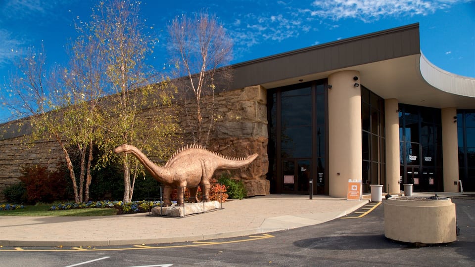 A dinosaur statue in front of a museum with a stone facade and large windows.