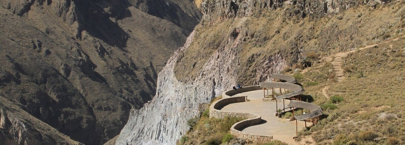 Paisagem montanhosa com um caminho sinuoso que leva a uma série de construções.
