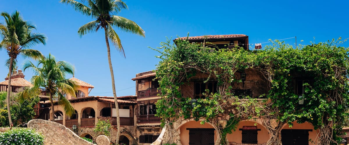 A historic building with arched doorways, palm trees, and a cobblestone courtyard.