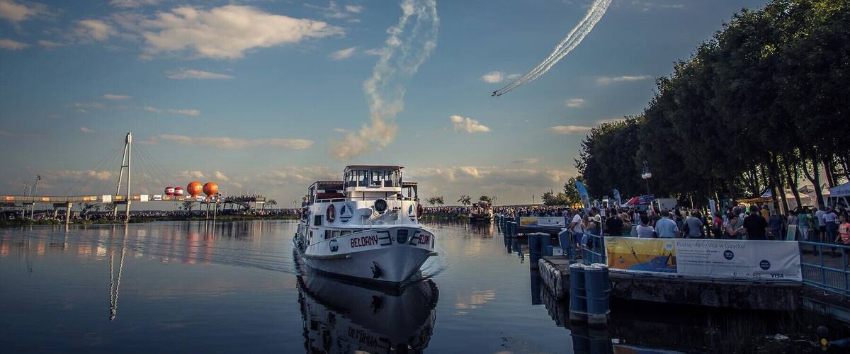 A boat named BELDRY with a white hull and red accents, docked at a pier with a crowd of people.