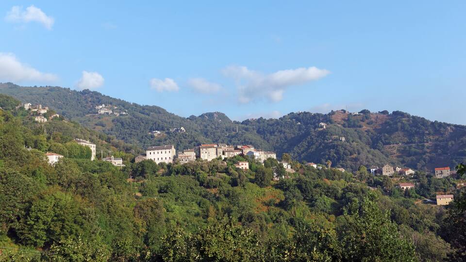 A hillside village with buildings nestled among trees and hills.