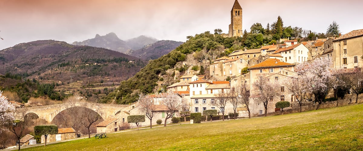 A historic town with a prominent church tower, a stone bridge, and lush greenery.