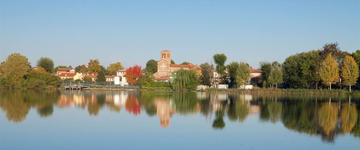 A calm lake with a church and residential buildings reflected in the water.