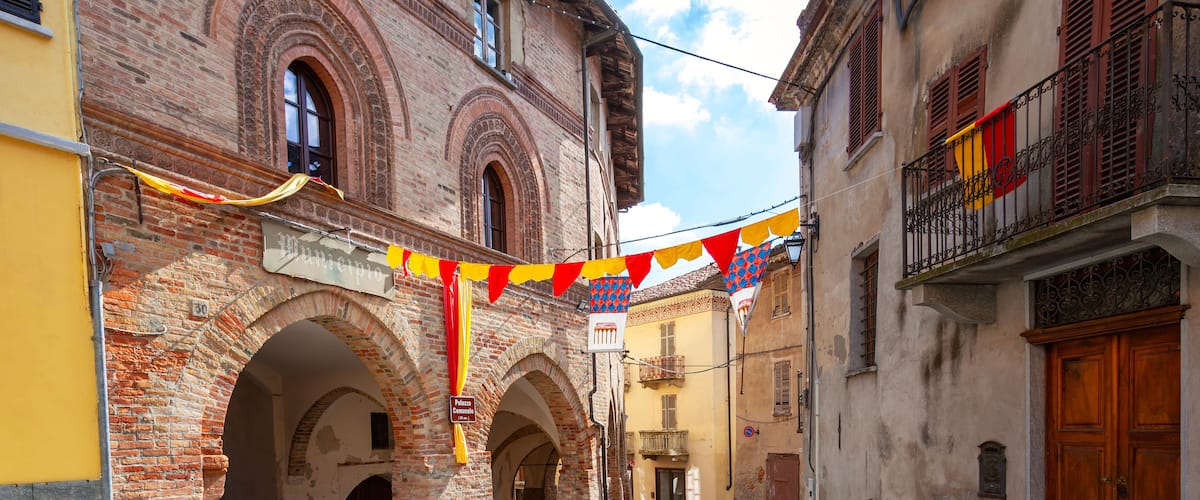 A cobblestone street with historic buildings, arches, and a flag.