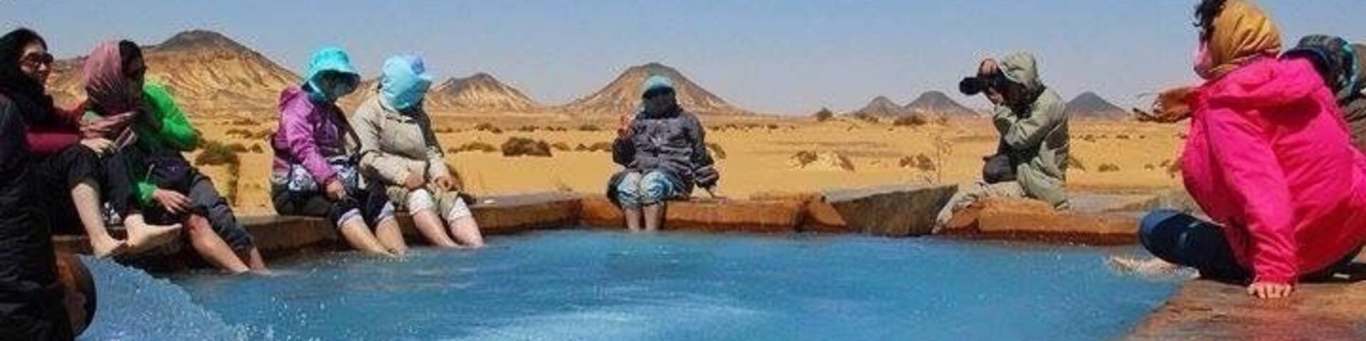 A group of people sitting around a small pool in a desert landscape.