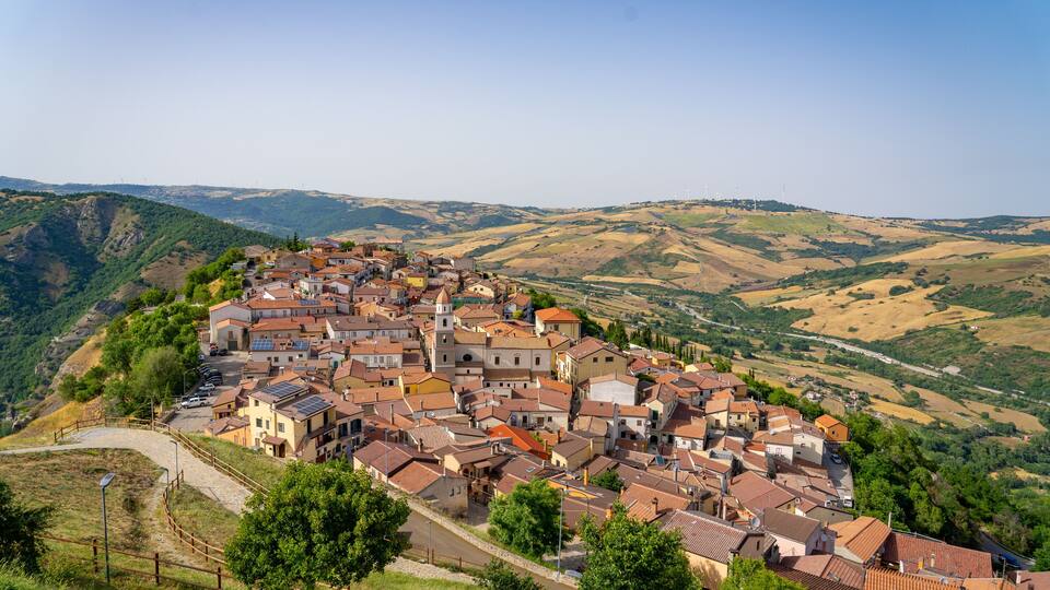 A hillside village with terracotta-roofed buildings, a prominent church, and rolling hills in the background.