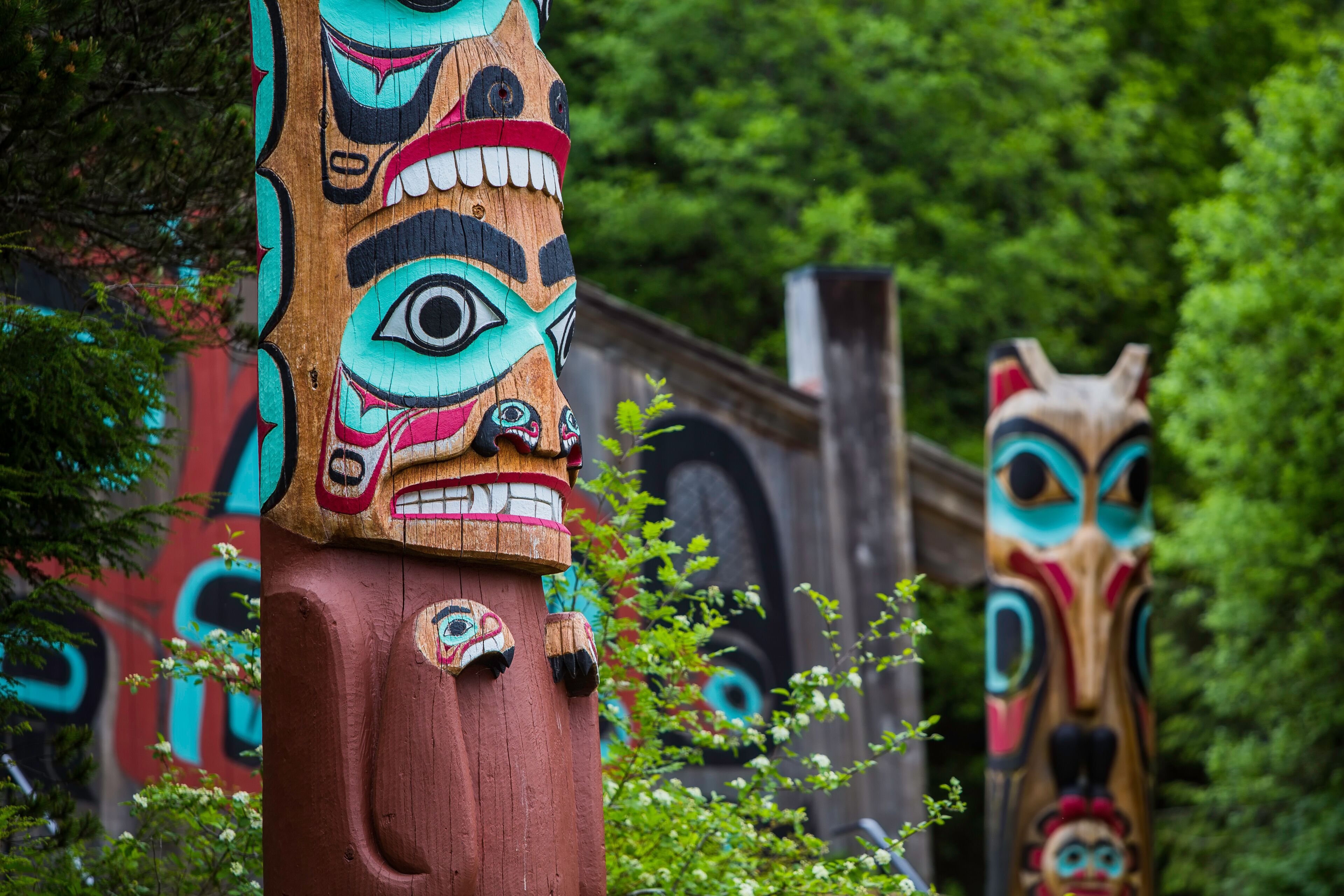 Two totem poles with intricate carvings and a lush green forest background.