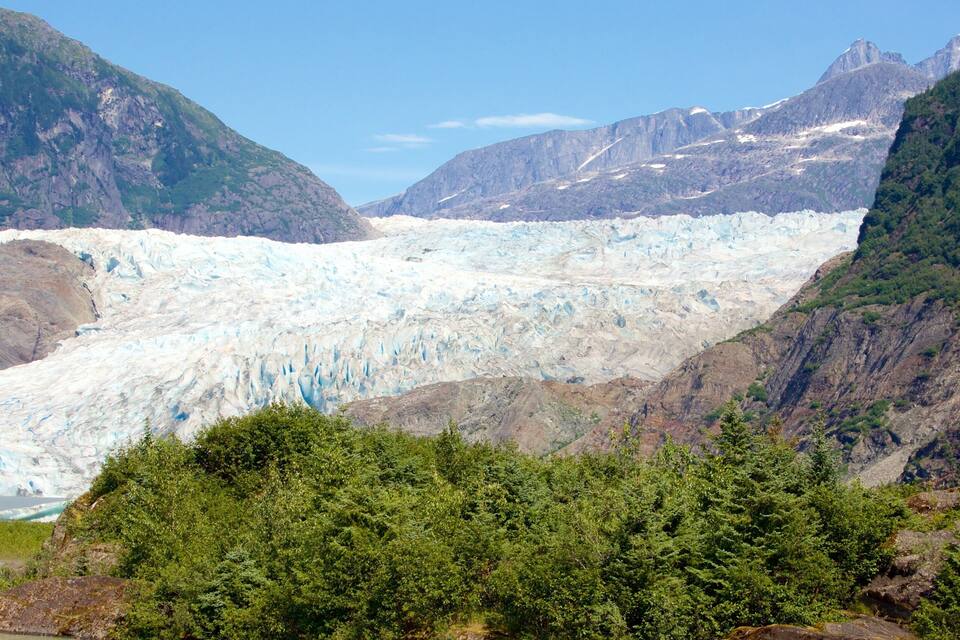 Un glaciar con un valle boscoso y montañas al fondo.