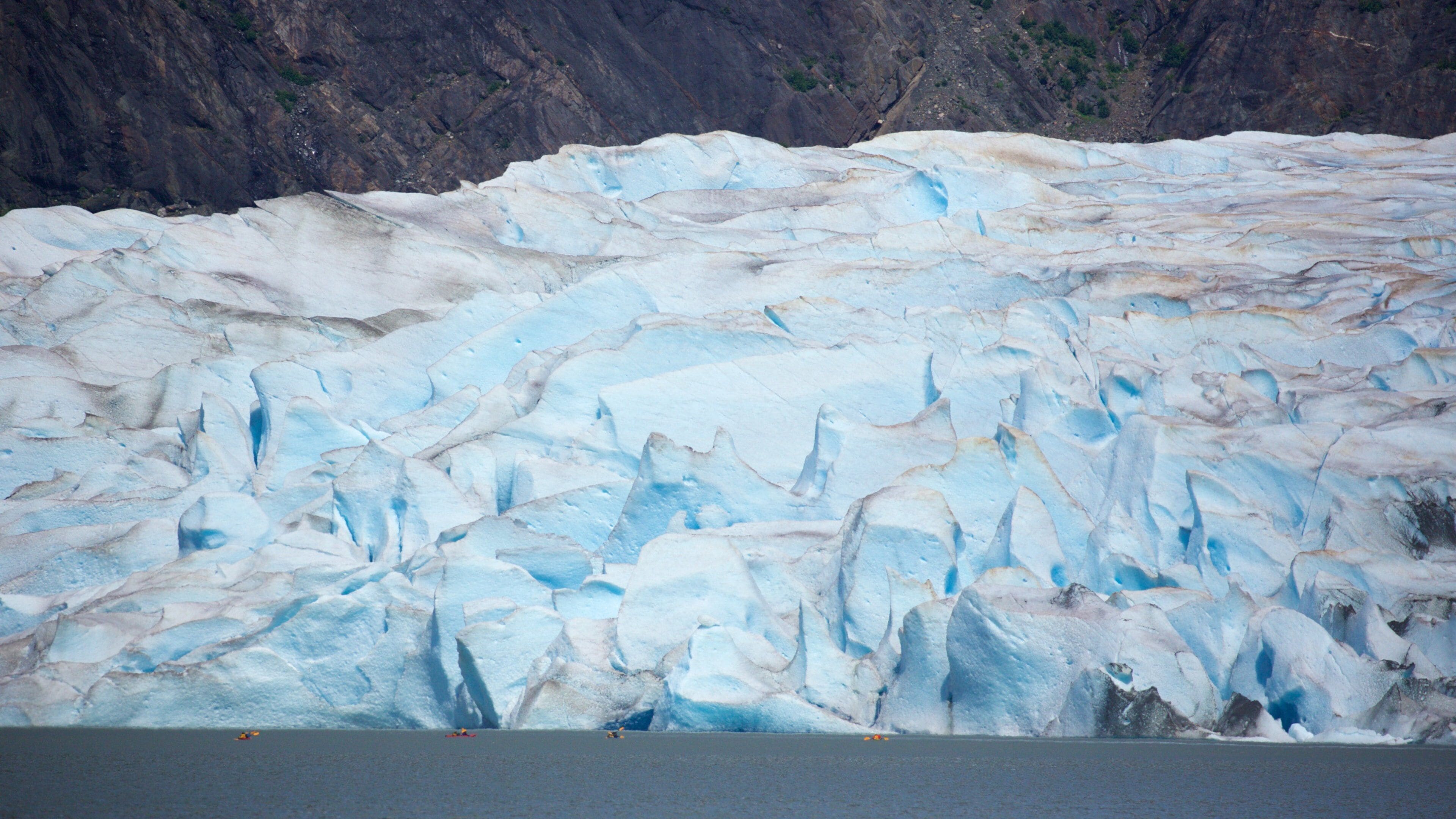 Un glaciar con grietas visibles y una pequeña embarcación en primer plano.