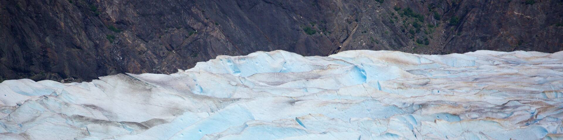 A glacier with visible crevasses and a small boat in the foreground.