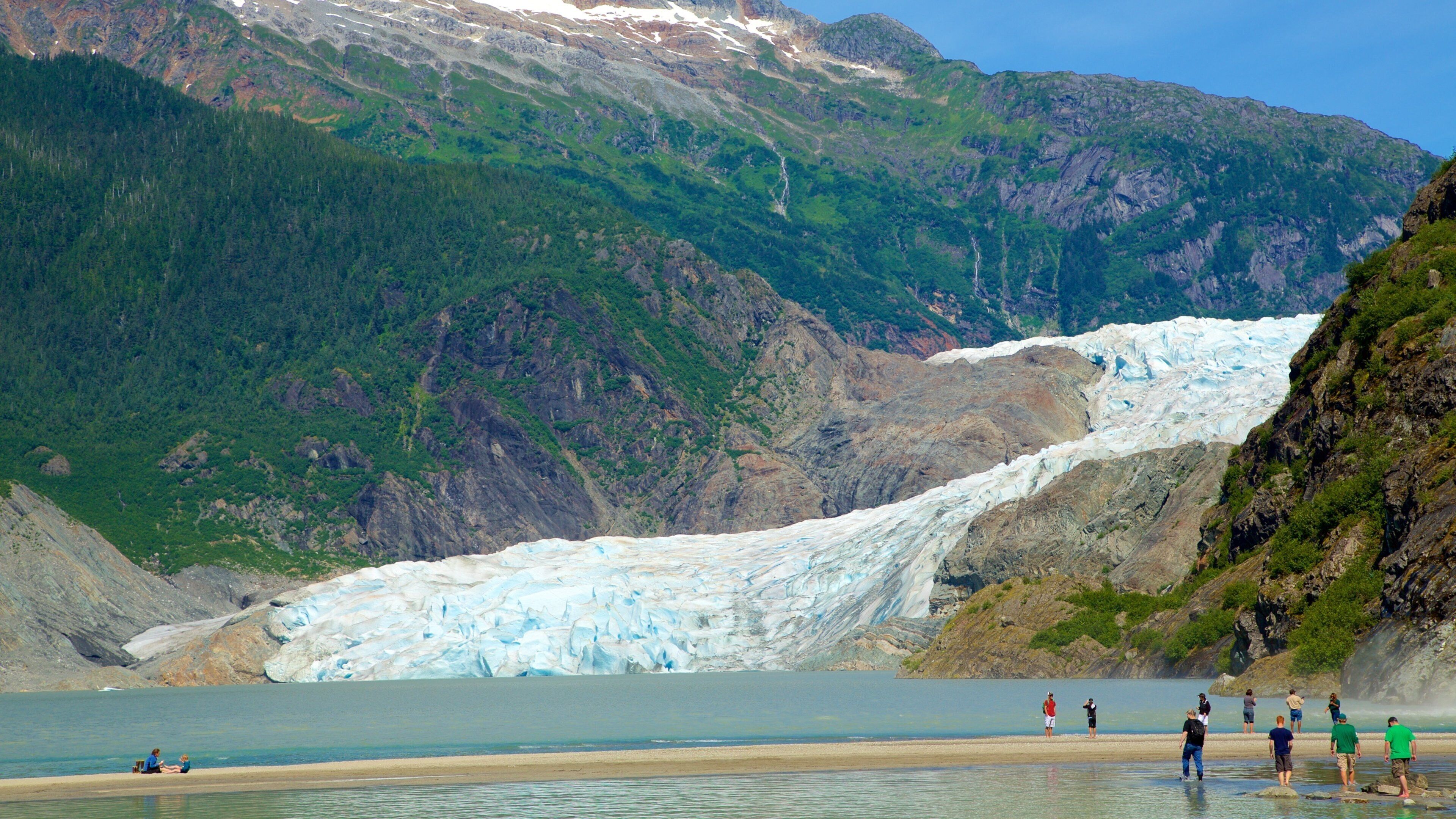 A glacier in a mountainous area with a lake and people observing.