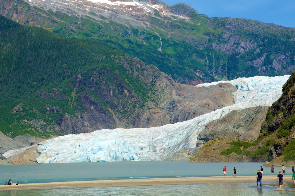 A glacier in a mountainous area with a lake and people observing.
