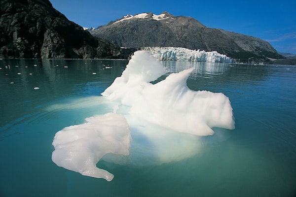A glacier with icebergs floating in a turquoise lake, surrounded by mountains.