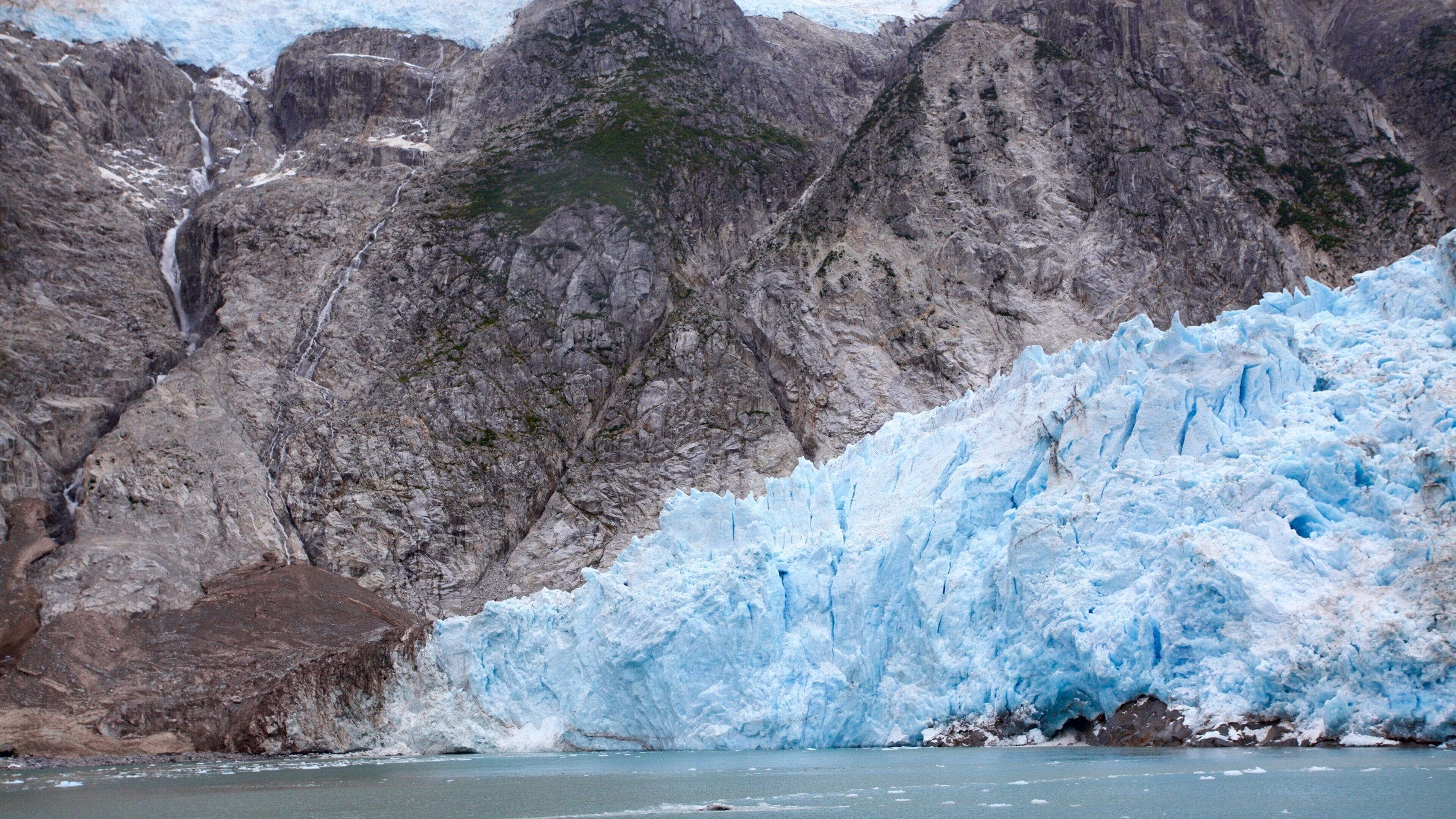 A glacier with a steep, rocky mountain backdrop.
