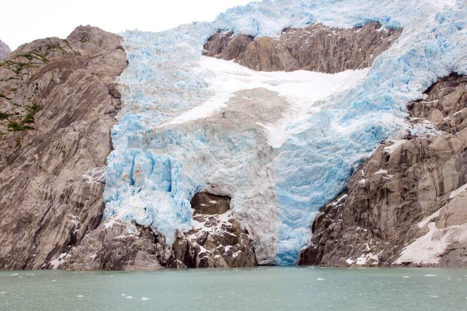 A glacier with a crevasse, rocky cliffs, and a body of water.