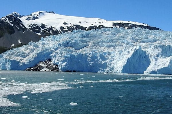 A glacier with a large ice calving into a body of water, surrounded by mountains.
