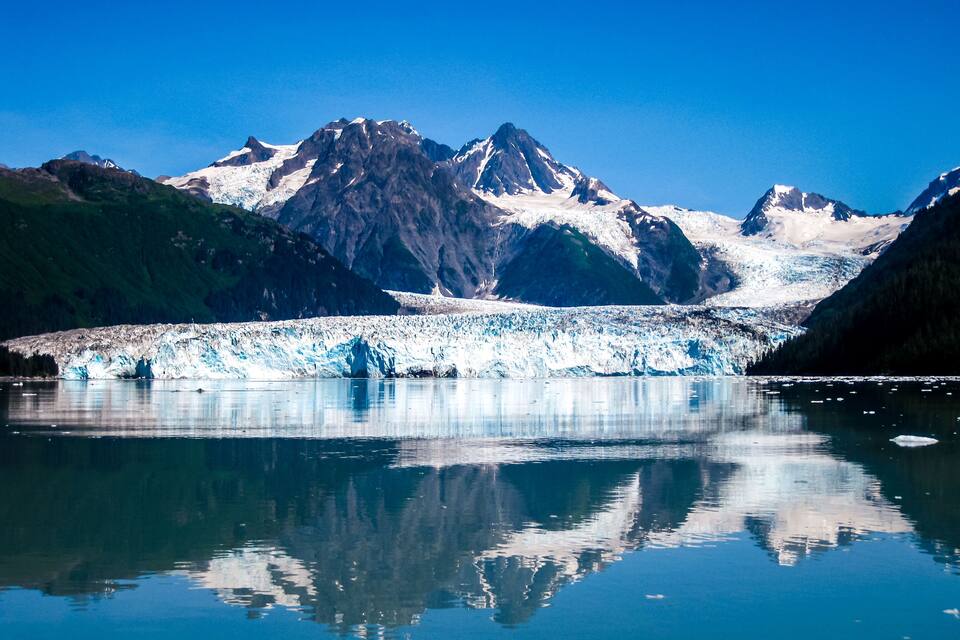 A glacier in a mountainous landscape with clear reflections in the water.