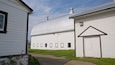 A white barn with a metal roof and a smaller adjacent building with a gable roof.