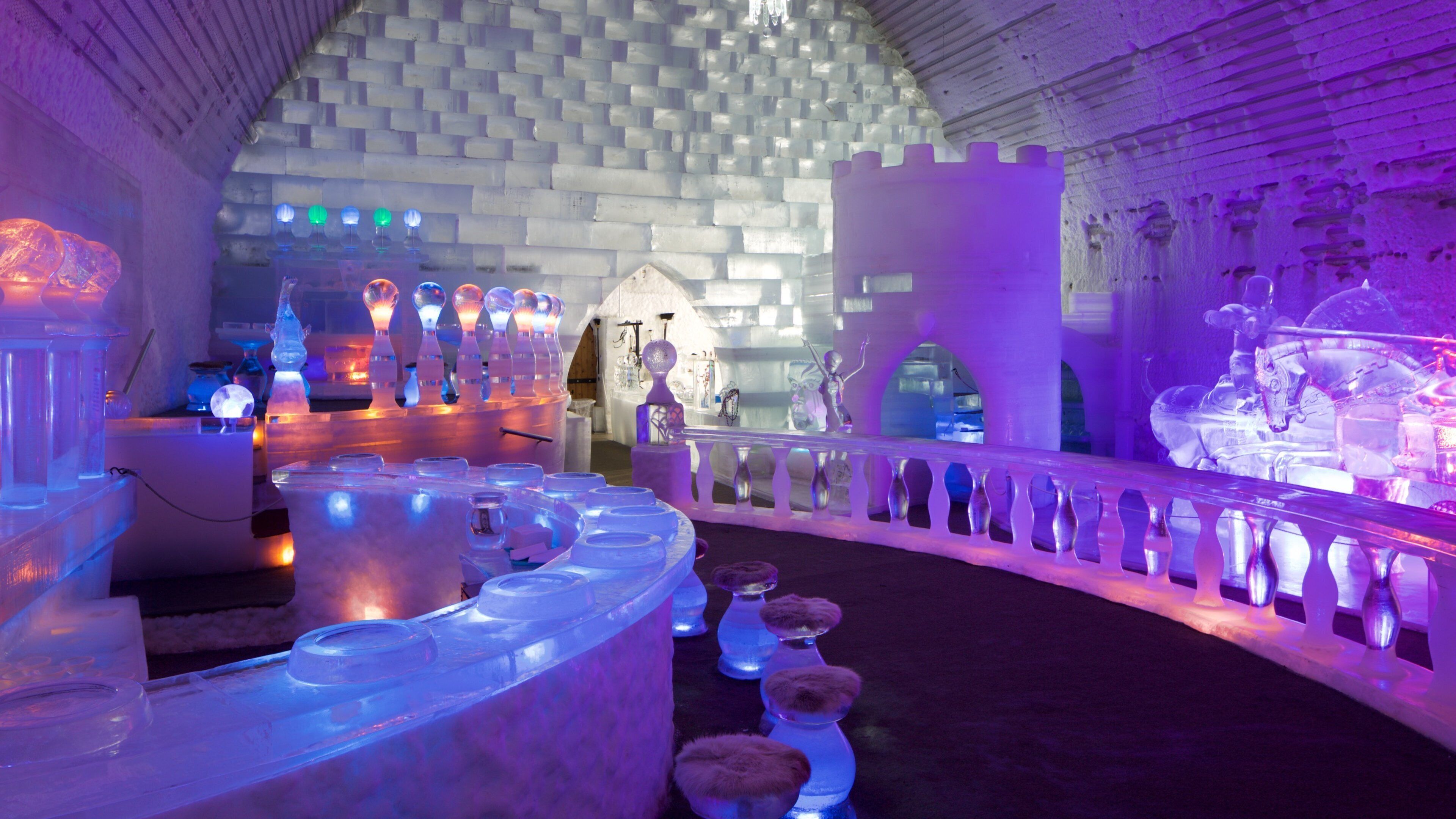 An ice bar with illuminated ice sculptures and a castle-like structure in the background.