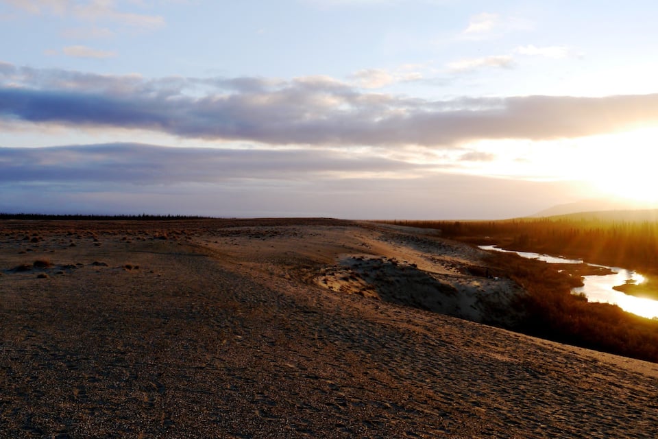 A river winding through a barren landscape with a sunset in the background.