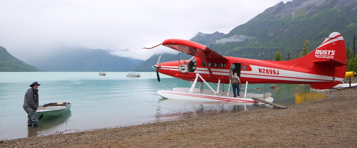 A red seaplane with the registration N2899J parked on a lake with mountains in the background.