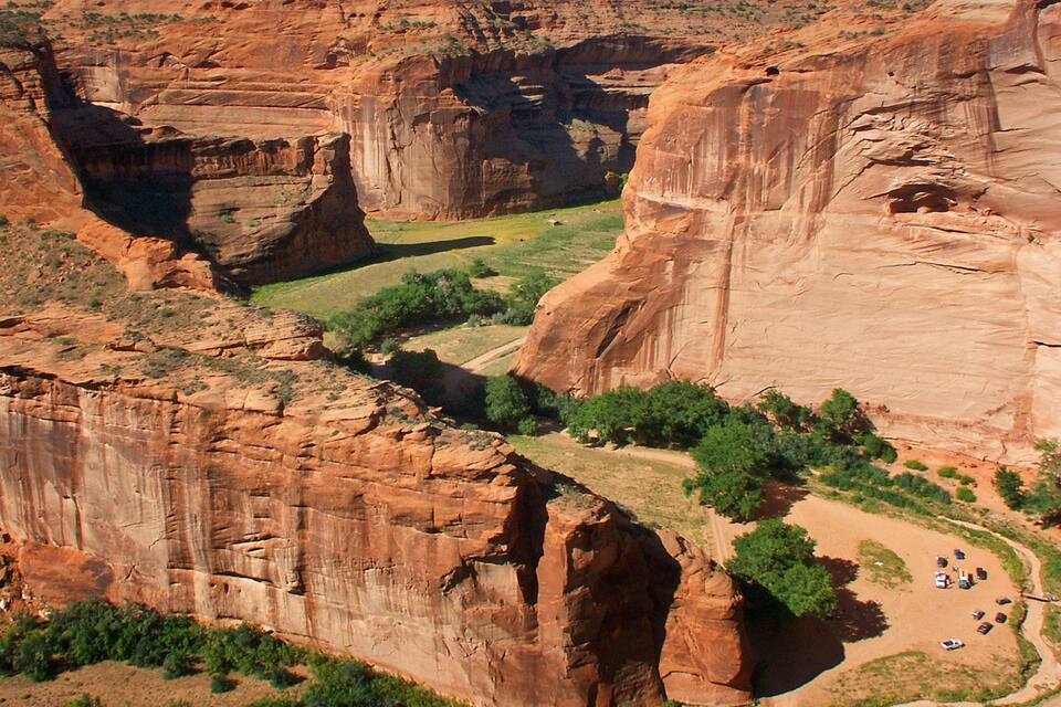 A canyon with red rock formations, a river, and a campsite.