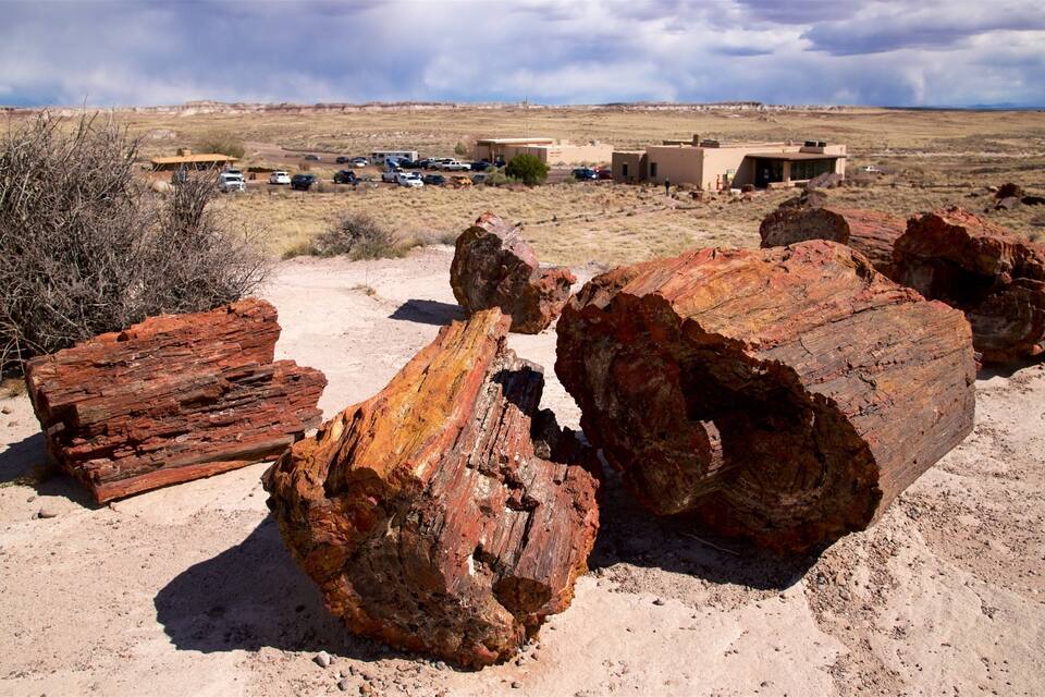 Large red rock formations in a desert landscape with a building and parked cars in the background.