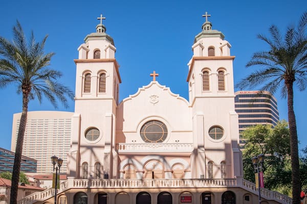 A pink church with two towers and a central dome, surrounded by palm trees and modern buildings.