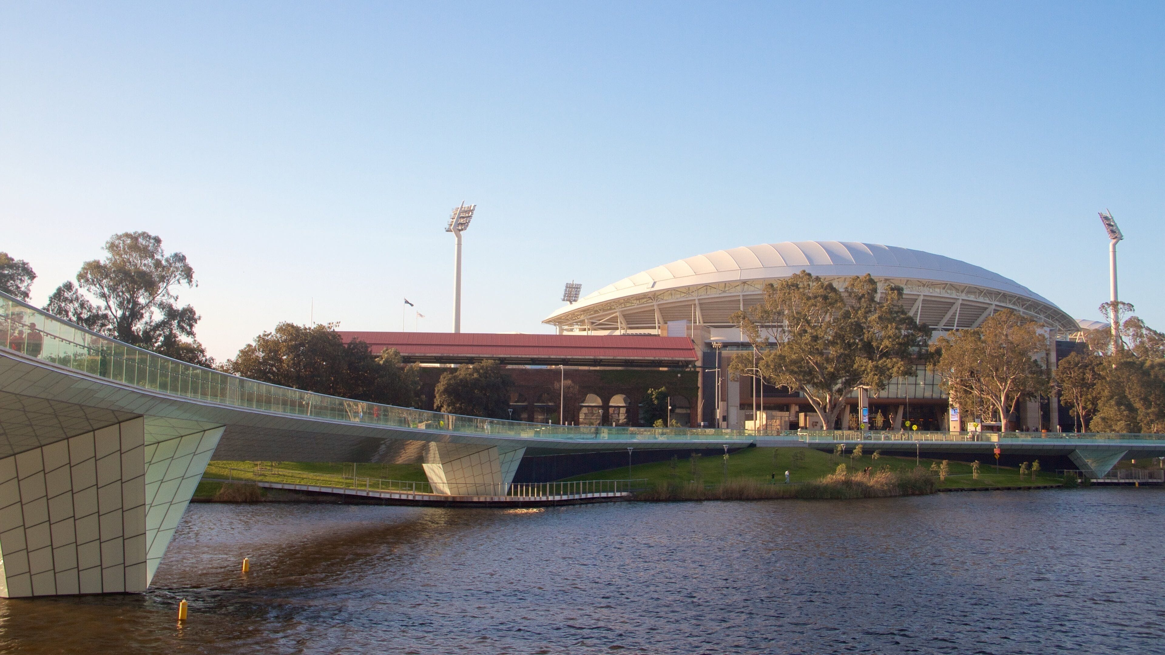A modern bridge over a river, a stadium with a distinctive dome, and surrounding greenery.