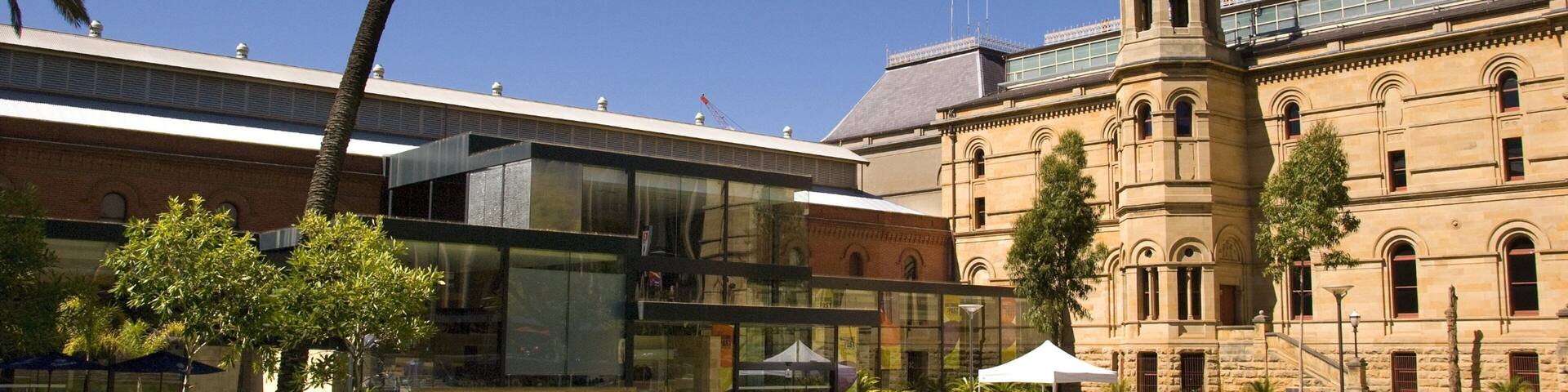 The South Australian Museum with a modern glass building and a historic stone building with a tower.