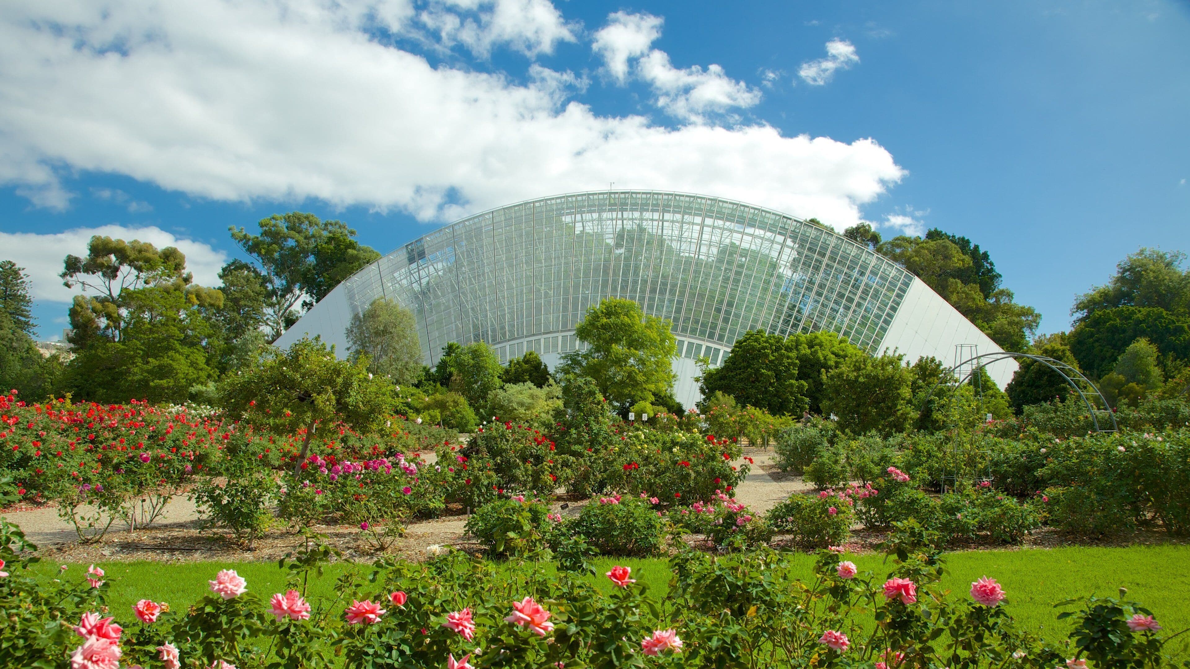 A large glass greenhouse surrounded by lush gardens and trees.