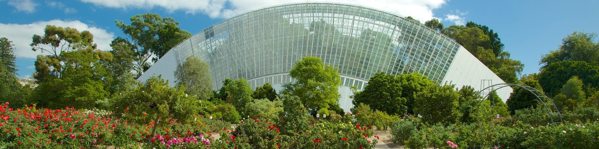 Un invernadero de vidrio grande rodeado de exuberantes jardines y árboles.