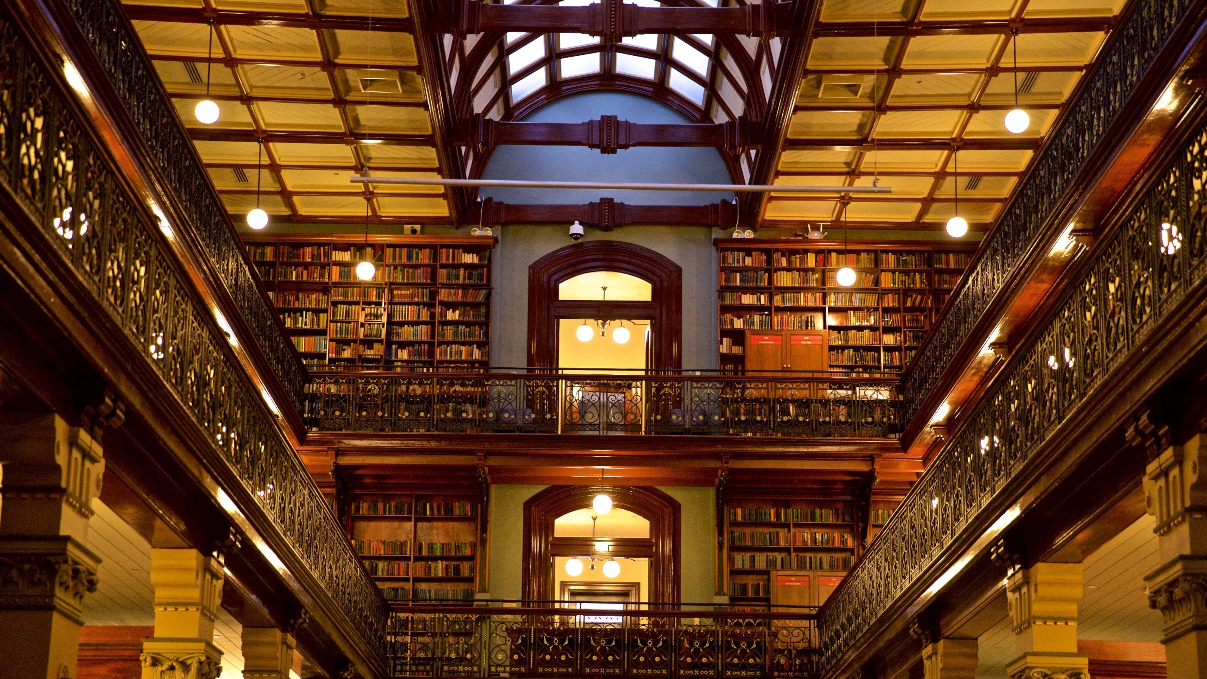 A grand library with ornate iron railings, wooden bookshelves, and a high, vaulted ceiling with skylights.