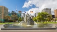 A city fountain with water jets, surrounded by trees and buildings.