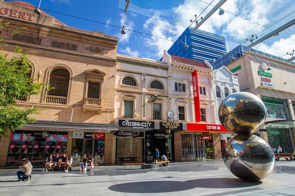 A city square with historic buildings, a large reflective sculpture, and various shops including a hair salon and a jeweler.