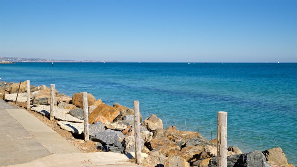 A rocky shoreline with a clear blue sea and a distant cityscape.