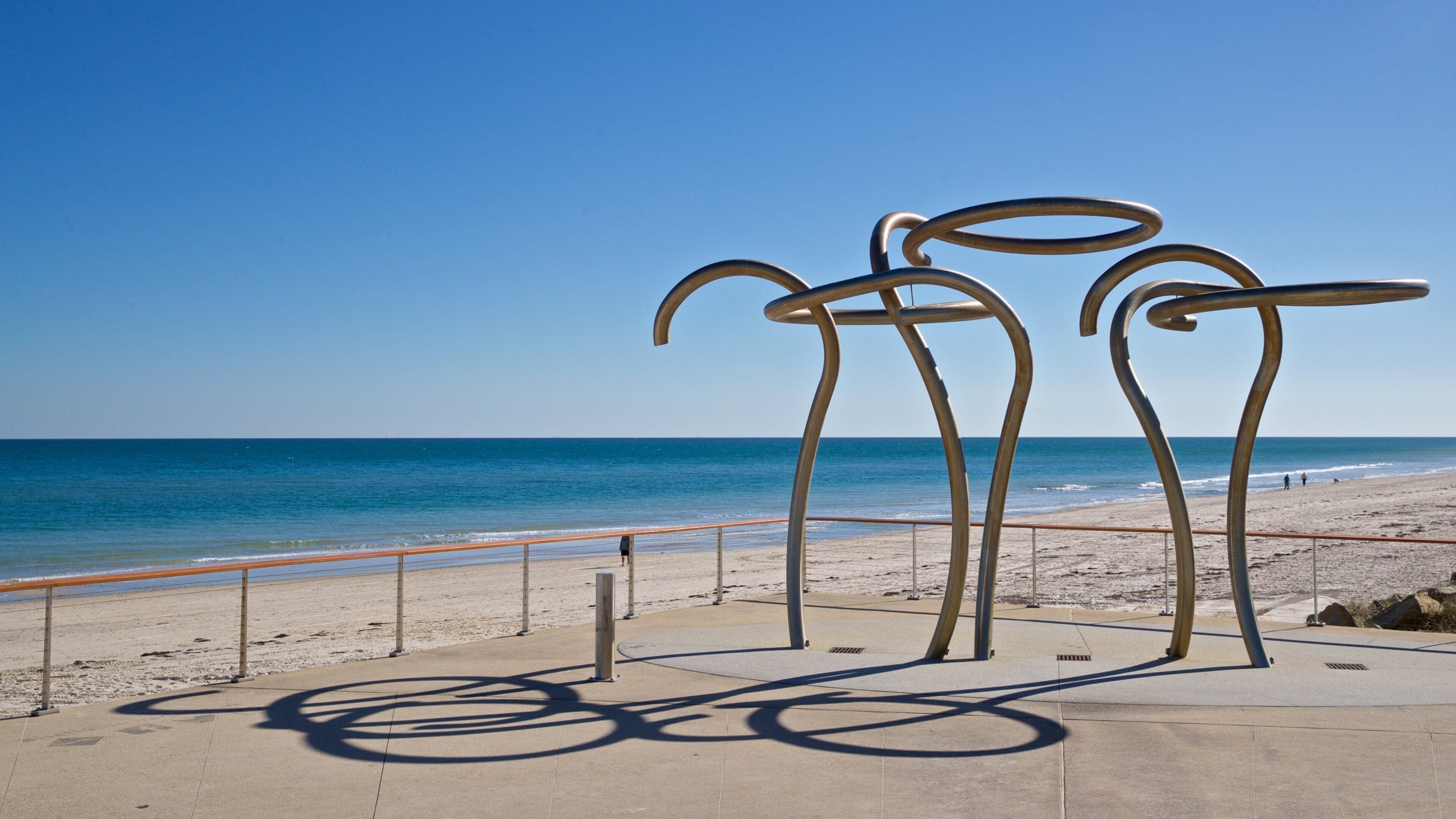 Une plage parsemée de sculptures métalliques, sous un ciel d’un bleu limpide.