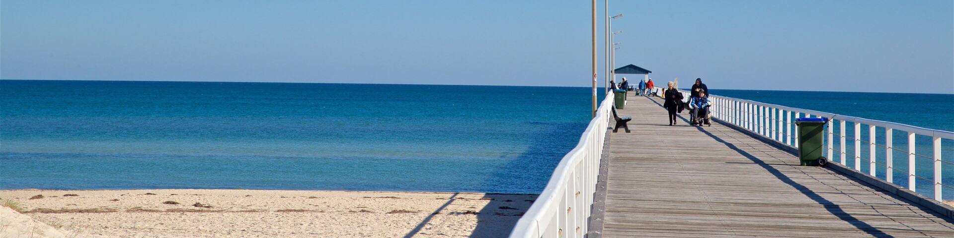 A wooden boardwalk extending to the beach with clear blue water and a sandy shore.