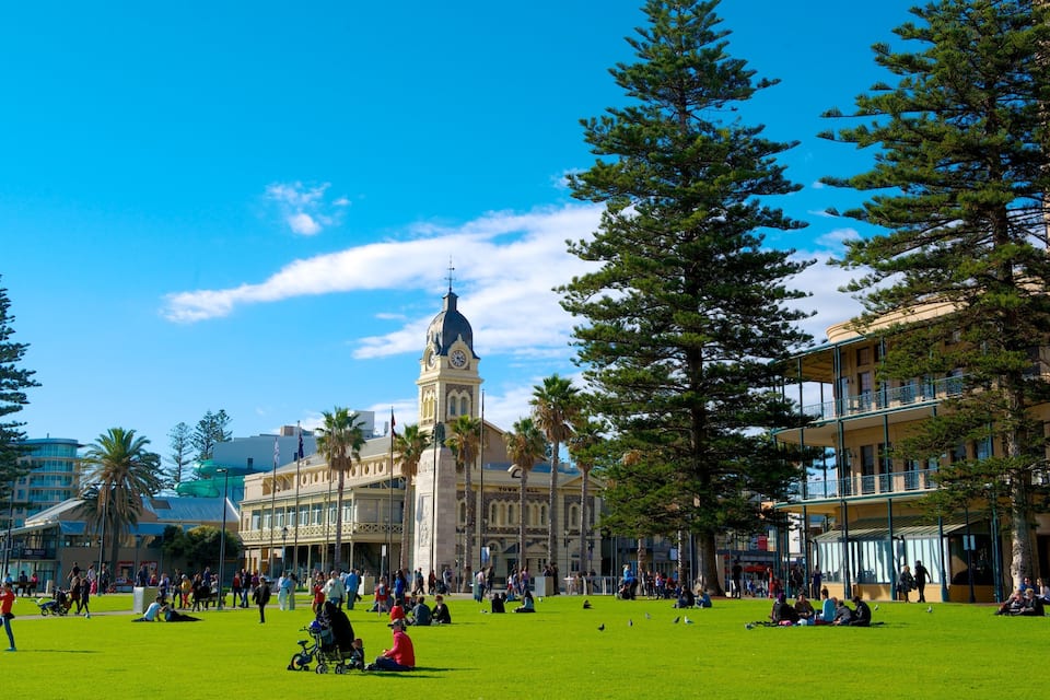 A public square with a prominent clock tower, surrounded by trees and buildings.