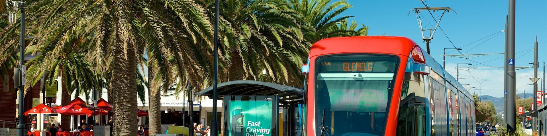 A tram at a station with palm trees and outdoor seating.