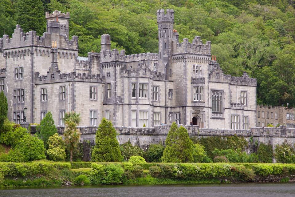 Un grande e storico castello con numerose torri e merli, circondato da vegetazione rigogliosa e un corpo d'acqua.
