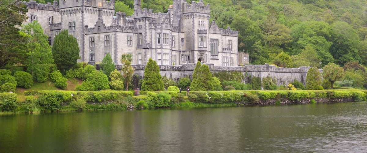 Ein großes, historisches Schloss, umgeben von üppigem Grün und einem stillen See.