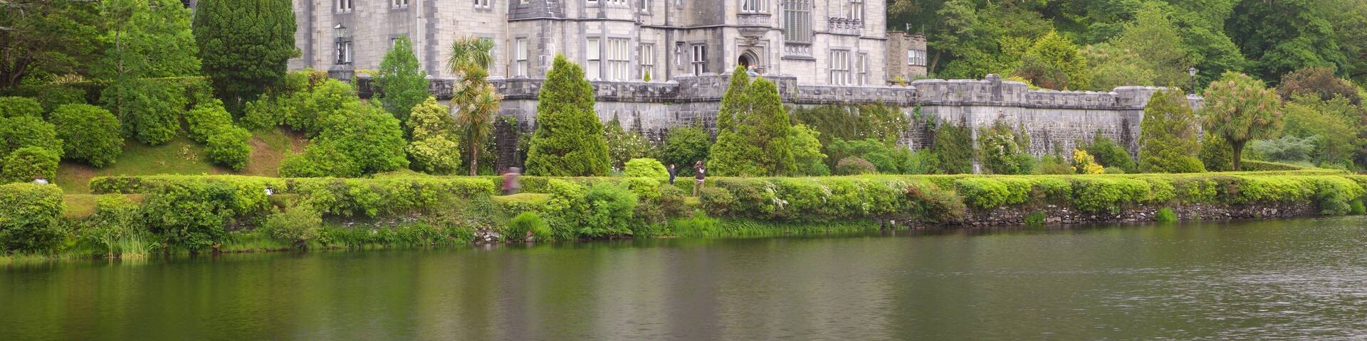 A large, historic castle surrounded by lush greenery and a calm lake.