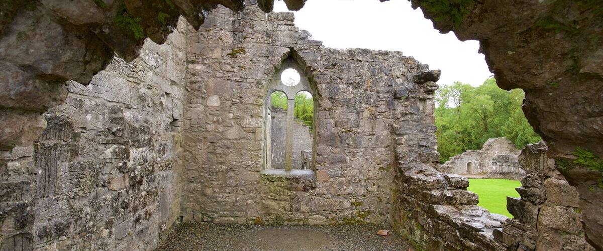 A stone archway with a circular window, surrounded by ruins and greenery.
