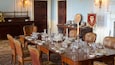 A formal dining room with a long wooden table set for a meal, surrounded by leather chairs with gold embroidery.